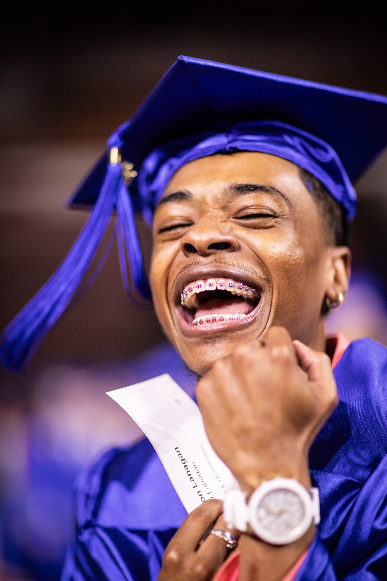 graduate wearing blue cap and watch with braces on teeth